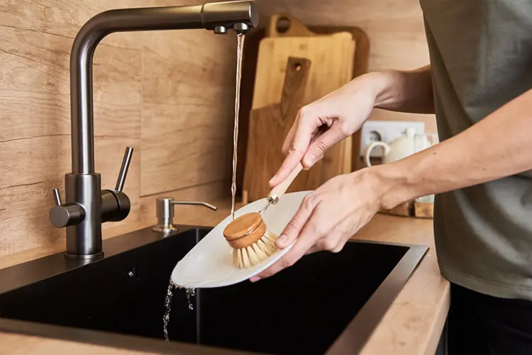 Woman washing dishes with eco-friendly wooden brush