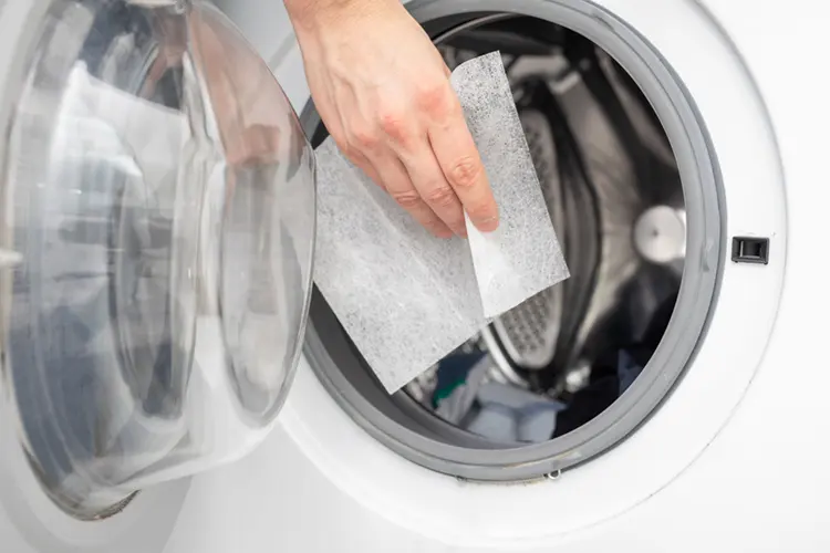 Woman inserting a laundry detergent sheet into a washing machine drum
